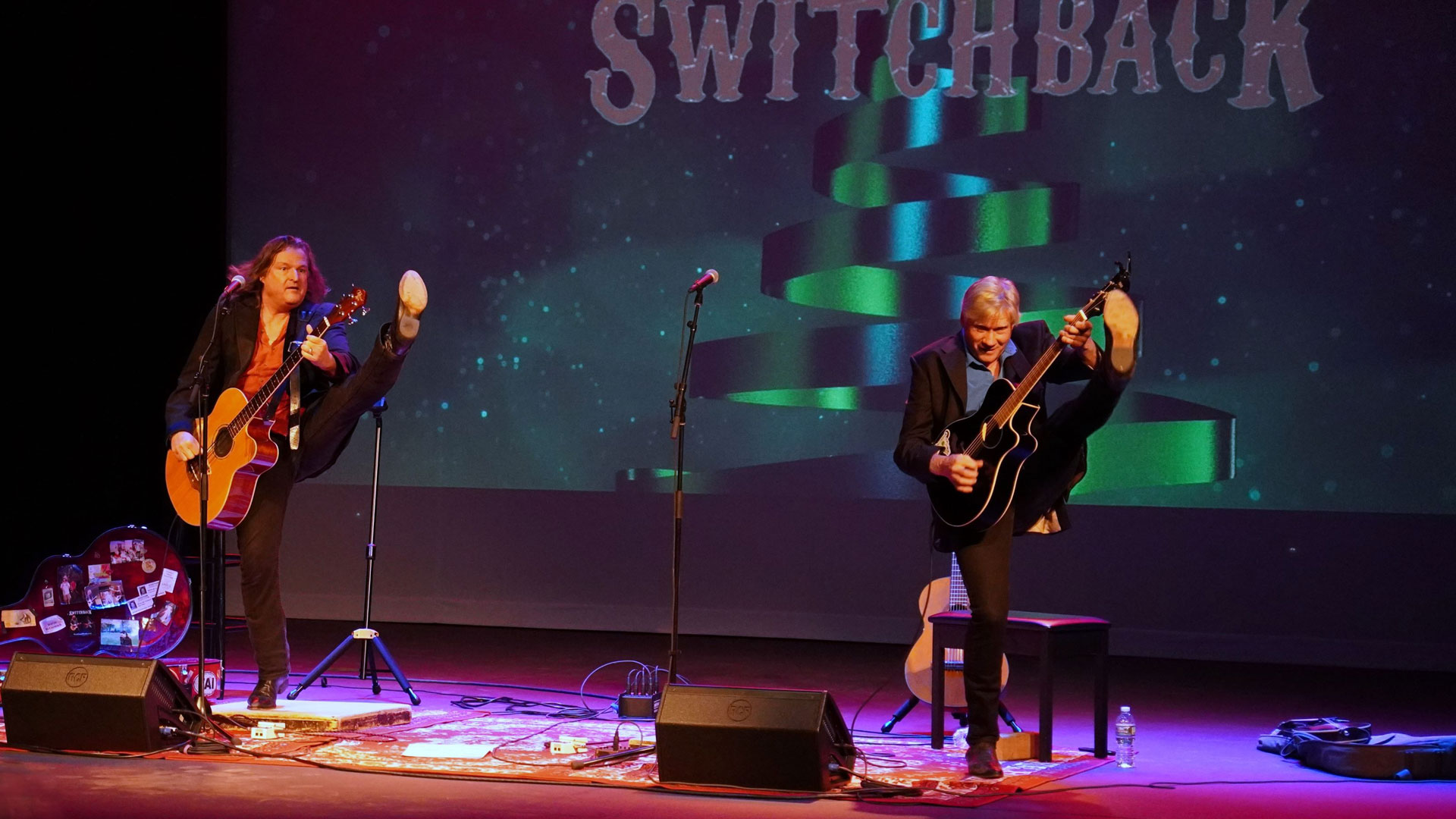 Switchback's Martin McCormick and Brian FitzGerald playing guitar and high kicking to Celtic Rock in their 2023 performance in Bay College's Besse Theater.