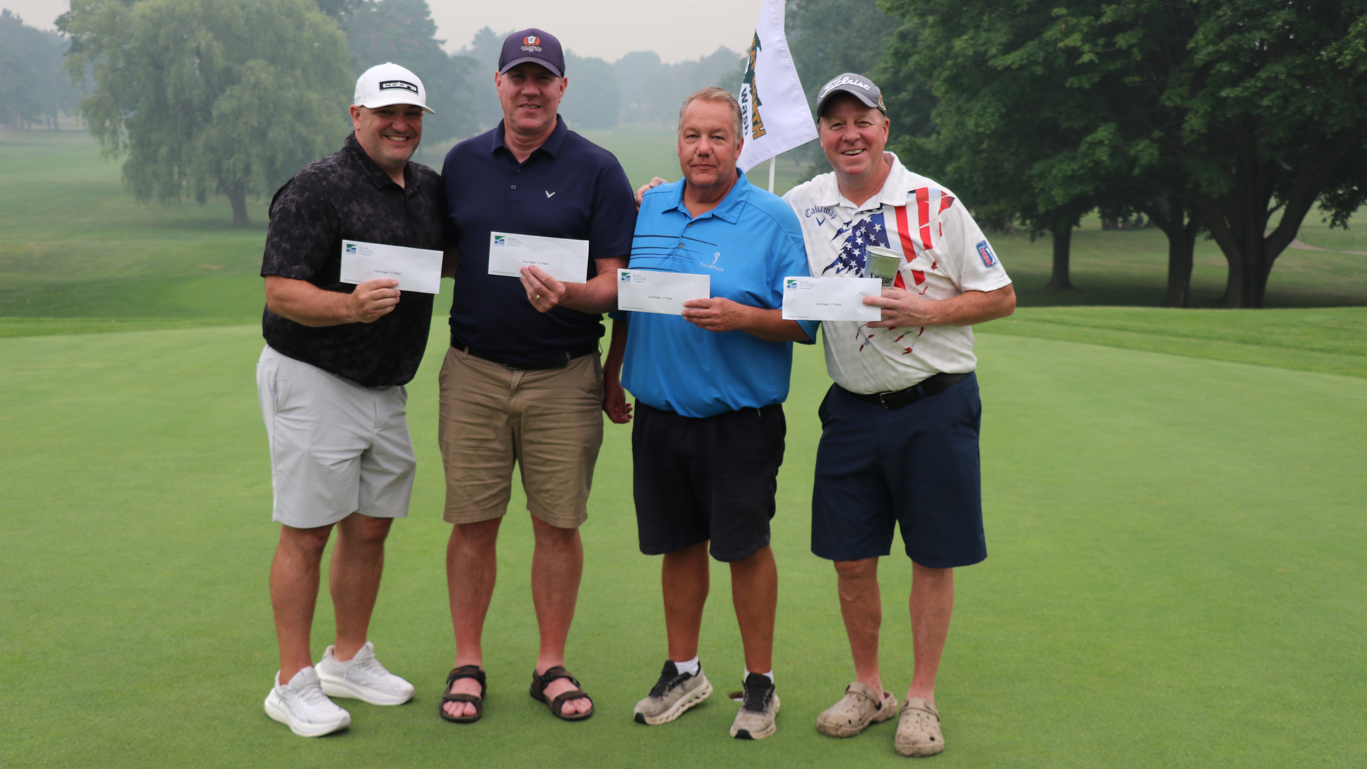 Four golfers pose smiling on the green at Escanaba Golf Course after the 35th Swing for Scholarships golf outing. Pictured from left to right are Jeff Erickson, Paul Rodman, Steve Scott, and Cory Kositzky.