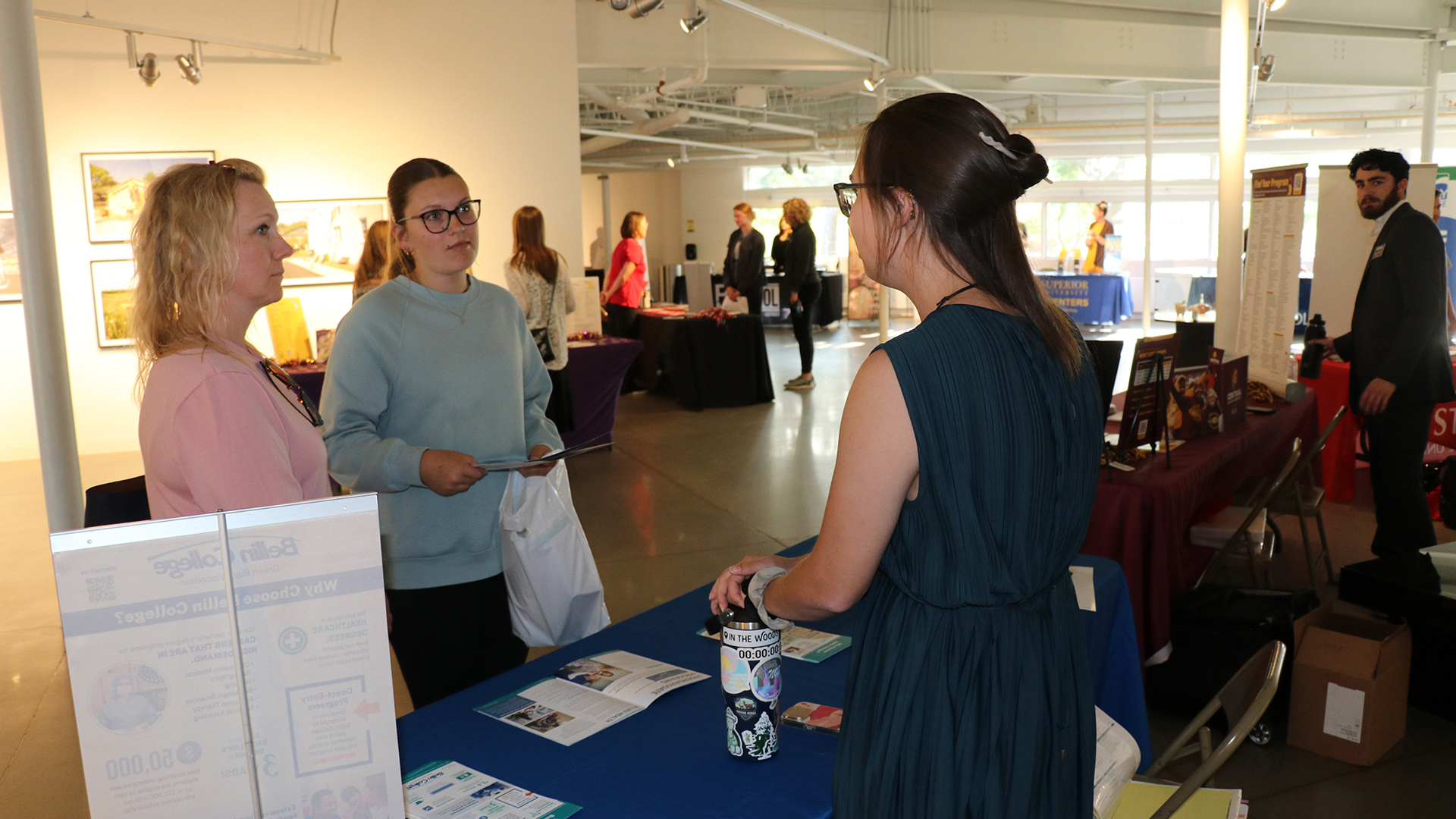 Two women attending College Night at Bay College in Escanaba speak to college representatives in the Besse Gallery in 2025.