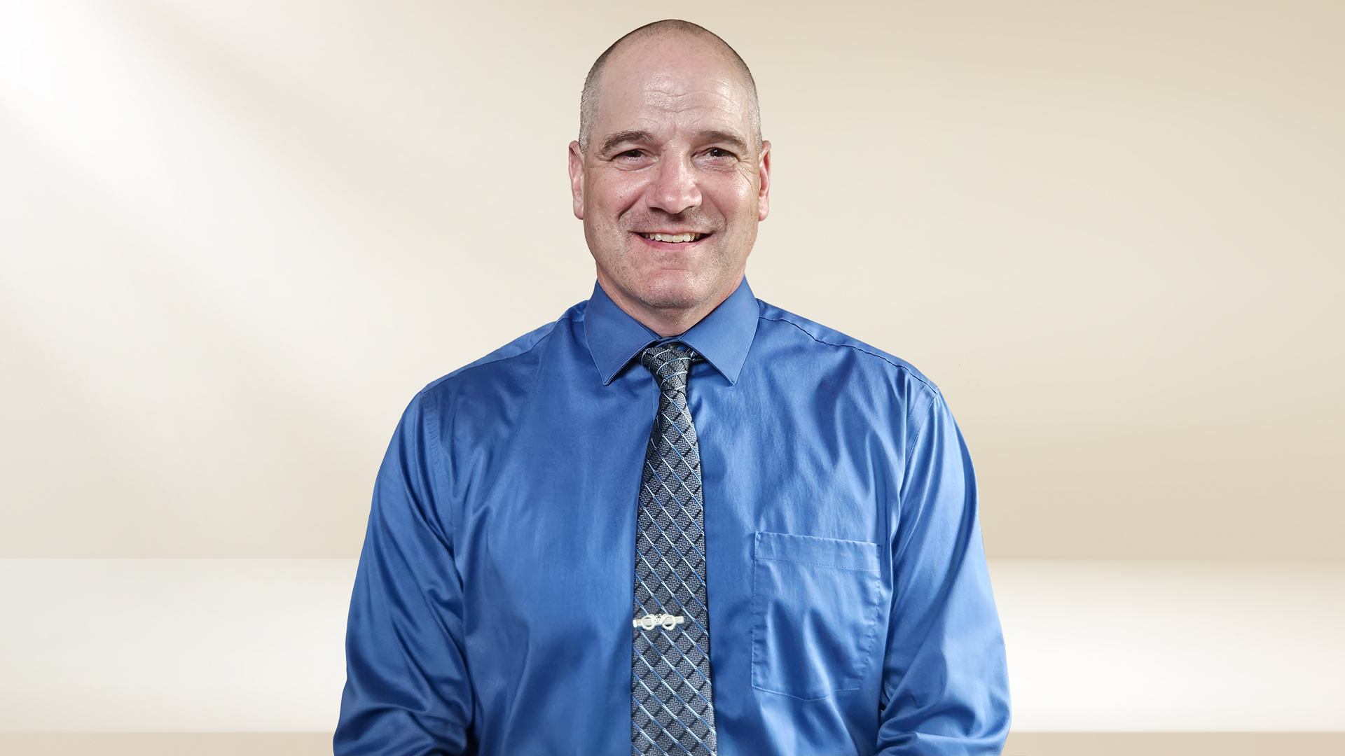 Joe Racicot smiling in a blue dress shirt and blue and gray tie.