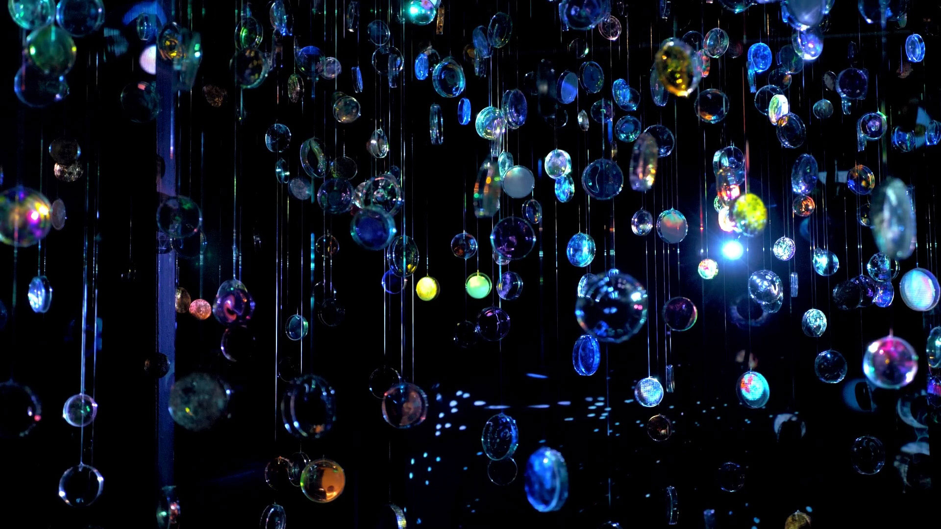 Art installation of hundreds of hanging glass orbs catching the light in a dark room.