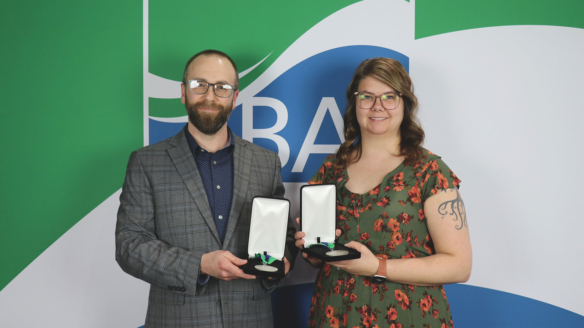 Kyle Schaeffer and Marie Johnson smiling in front of the Bay College logo while holding their award medals.