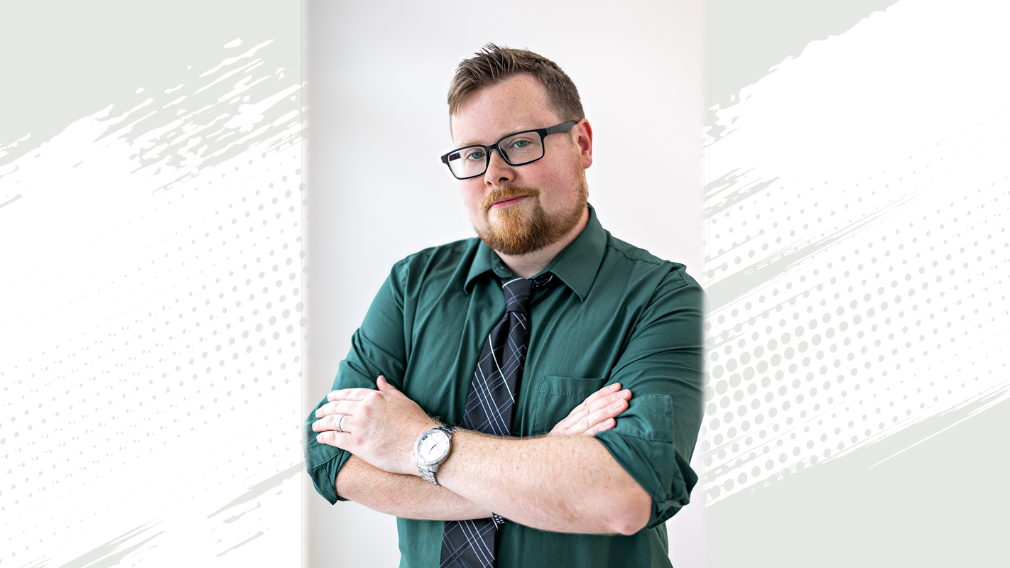 Coordinator of Campus User Technology and Bay College quarterly TORCH Award Winner Brian Schaefer in a gray collared shirt with black tie and black glasses.