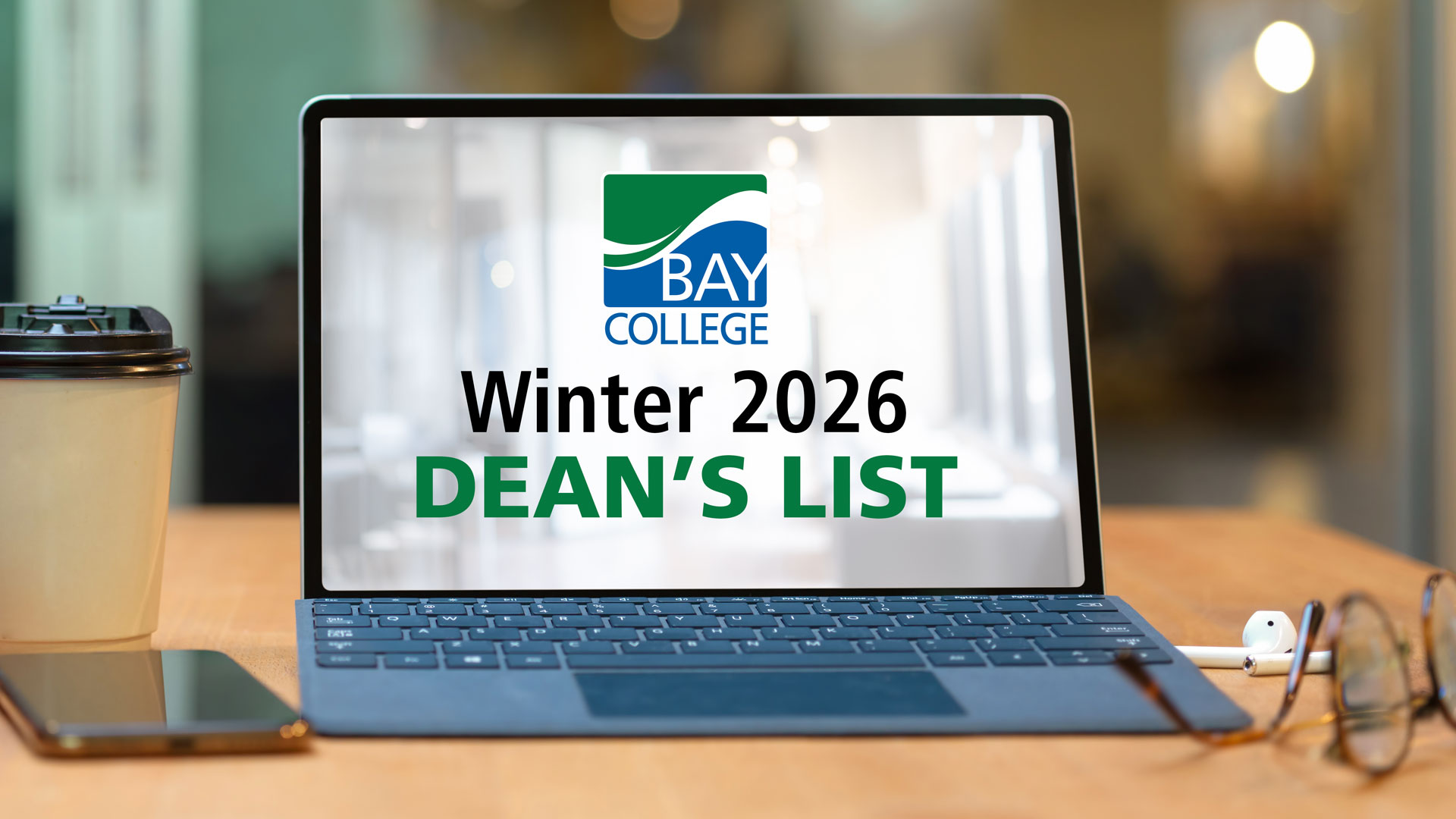 A laptop on a desk beside a cup of coffee, glasses, and Airpods. The screen has the Bay College logo above, "Winter 2026 Dean's List"