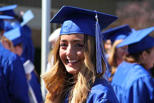 Smiling female graduate wearing a blue graduation cap and gown