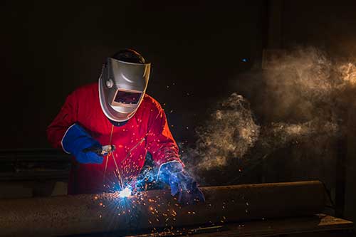 Welder bonding metal with welding device in workshop, lots of sparks to be seen, he wears welding goggles