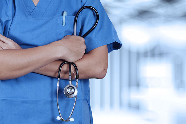 Close-up of nurse wearing blue scrubs holding a stethoscope.