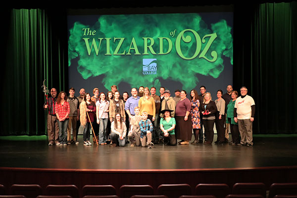 The Production Team of The Wizard of Oz stand below backdrop of Wizard of Oz lettering in green