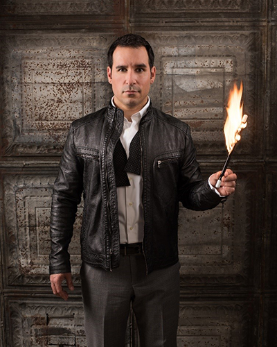 Daniel Martin stands in leather jacket and holds torch.