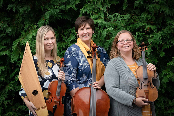 Trio members are pictured against a natural green backdrop and are each holding instruments.