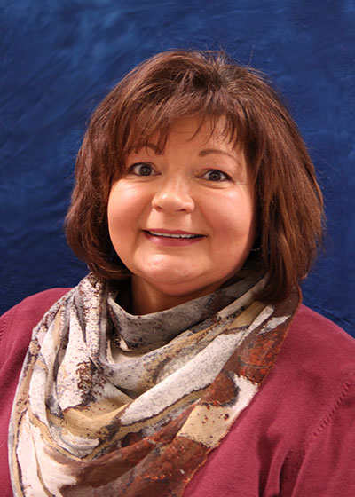 Sue Sundstrom-Young is pictured in a maroon sweater and scarf against a blue background.