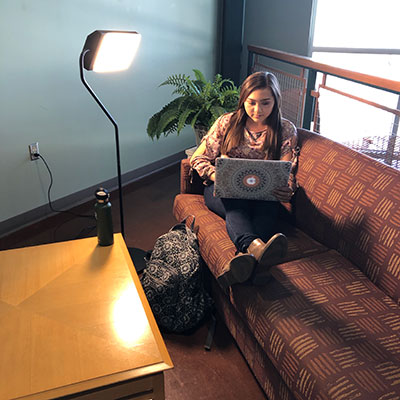 Female student pictured on couch with lap top under sun lamp.