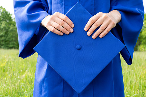 Graduate holding a blue graduation cap