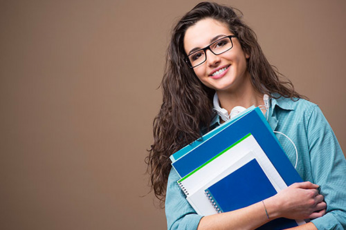 Smiling female college student holding books isolated on a brown background