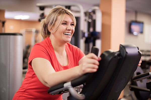 Happy woman riding on exercise bike at the gym